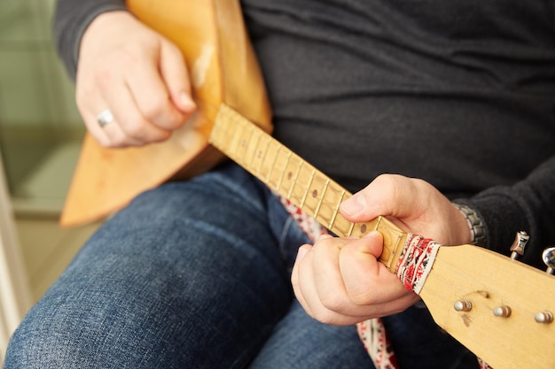 As mãos dos homens tocam a balalaica um instrumento musical de cordas folclóricas russas com um corpo triangular com três cordas