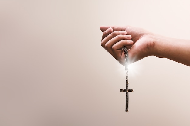 As mãos em oração seguram um crucifixo ou uma cruz de colar de metal com fé na religião e crença em Deus. Poder da esperança e devoção.