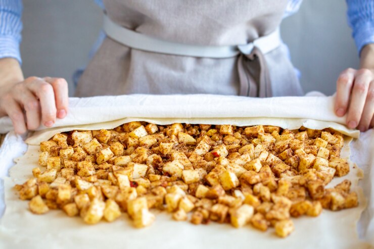 Foto as mãos envolvem a massa com recheio de maçã e fazem strudel de maçã