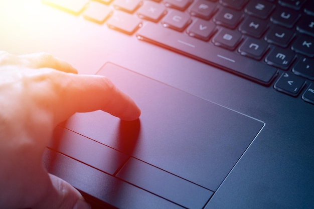 As mãos estão usando um touchpad de laptop fechando a imagem e a luz do sol