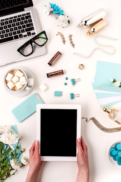 As mãos femininas e tablet contra objetos de mulher moda azul em branco. Conceito de maquete feminina