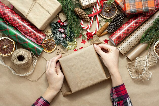 Foto as mãos femininas embalam e decoram um presente de natal, a mesa é coberta com papel artesanal bege e
