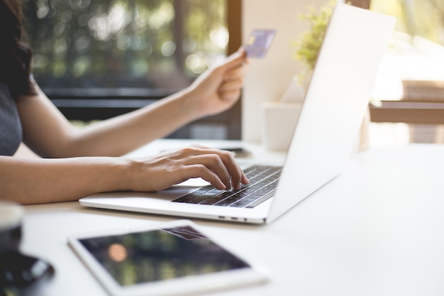 As mãos femininas seguram cartões de crédito e compram on-line através de laptops.