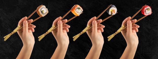 As mãos femininas seguram rolos de sushi com palitos. Parede preta. Conceito criativo.