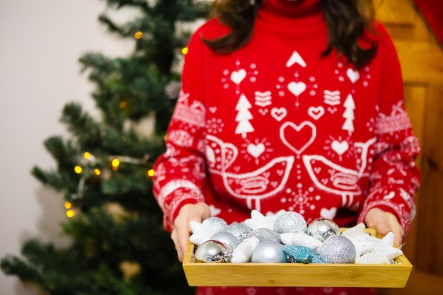 As mãos femininas seguram uma bandeja com muitos brinquedos para árvores de Natal. Processo de decoração de árvore de Natal. Natal de ano novo. 2022 ano do tigre.