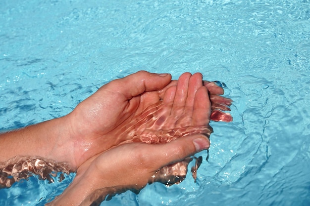 As mãos juntas submersas em água azul clara e limpa na piscina