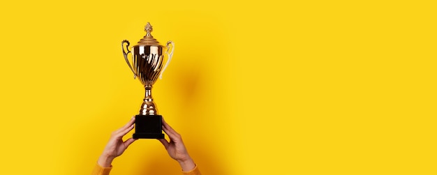 As mãos levantadas de uma mulher segurando um troféu sobre fundo amarelo