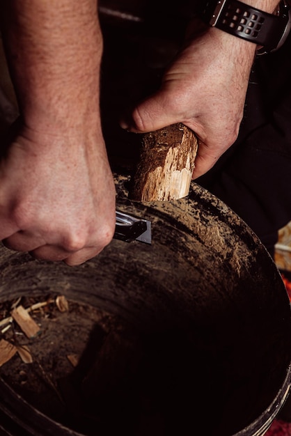 As mãos masculinas esculpem madeira com uma faca