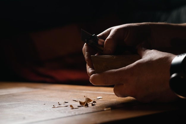 As mãos masculinas esculpem madeira com uma faca