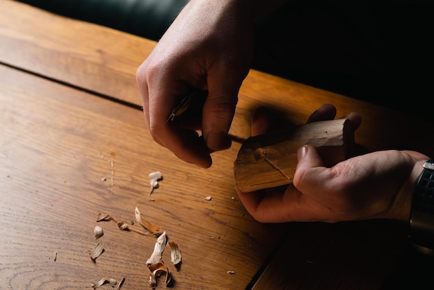 Foto as mãos masculinas esculpem madeira com uma faca