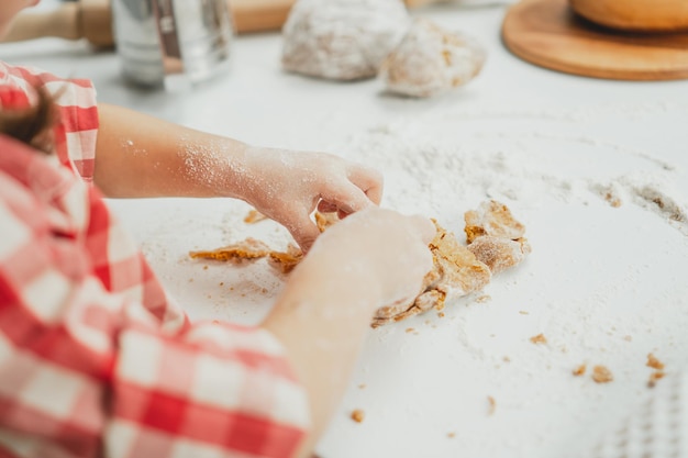 As mãos parcialmente desfocadas de uma menina com uma camisa quadriculada vermelha preparam a massa para biscoitos de gengibre na cozinha branca