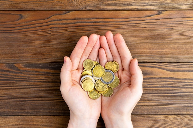 As mãos seguram a pilha de moedas de euro no fundo de madeira.