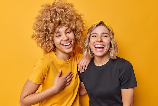 As melhores amigas riem alegremente se divertem sorrindo amplamente se divertem juntas vestidas com camisetas casuais isoladas sobre o fundo amarelo vívido do estúdio Conceito de emoções e sentimentos humanos positivos