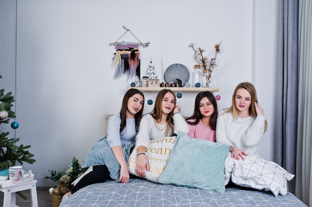 As meninas de quatro amigos bonitos usam camisolas quentes e calças pretas na cama no quarto decorado no estúdio, brincam com almofadas.