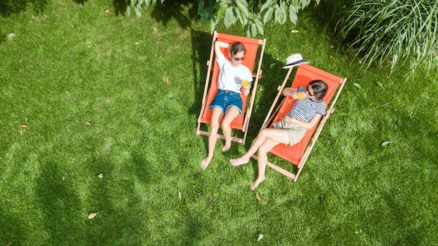 As meninas relaxam no jardim de verão em espreguiçadeiras na grama, amigas mulheres se divertem ao ar livre