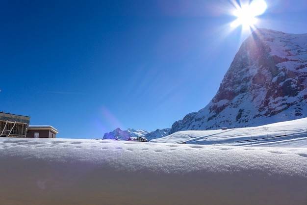 As montanhas são cobertas de neve no fundo do céu azul e da luz solar