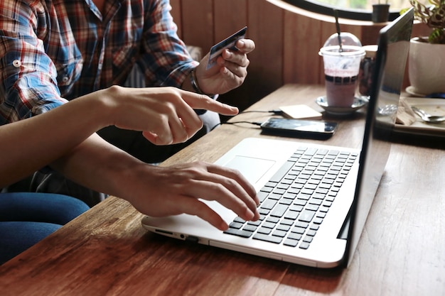 As mulheres apontam para encomendar homem compras on-line com cartão de crédito e laptop