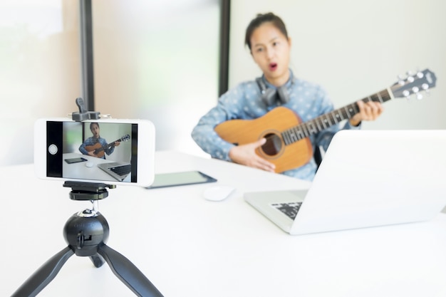 As mulheres cantam uma música com guitarra nas mãos usam câmera para transmitir vídeo ao vivo para redes sociais pela internet em casa.