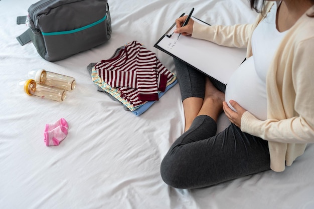 As mulheres grávidas ficam felizes em preparar roupas de bebê fazendo malas para ir ao hospital