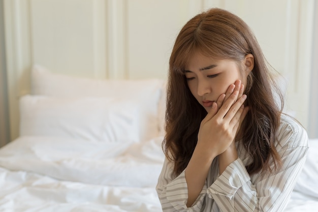 As mulheres jovens asiáticas têm dentes sensíveis, dores de dente, cáries ou gengivas inflamadas. Saúde e conceito de pessoas doentes.