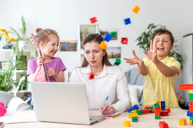 As mulheres jovens trabalham em casa com o laptop, junto com as crianças. as crianças fazem barulho