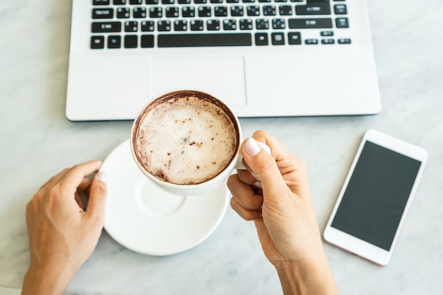 As mulheres seguram uma xícara de café enquanto olha para laptop no café.