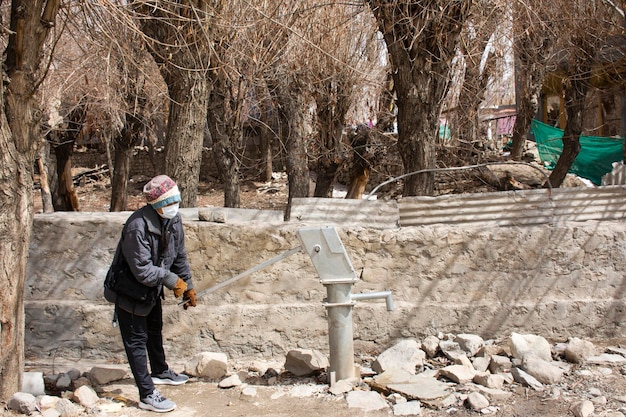 As mulheres tailandesas dos viajantes testam o uso da bomba manual de alavanca antiga do poço de águas subterrâneas ao ar livre no beco da vila de Ladakh no vale do Himalaia em Jammu e Caxemira na Índia durante a temporada de inverno