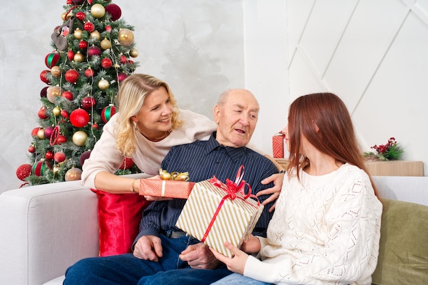 As netas dão um presente ao avô Homem sênior feliz abraçando sua neta enquanto recebe um presente no Natal em casa