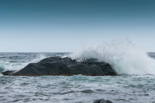 As ondas estão batendo contra rochas à beira-mar o oceano em tempo nublado