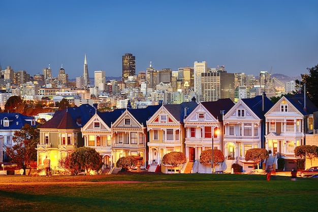 As painted ladies de san francisco, califórnia, brilham em meio a um pôr do sol e arranha-céus.