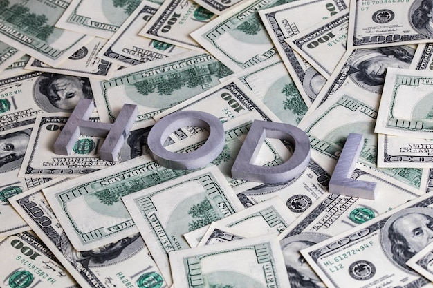 As palavras HODL colocadas com letras de alumínio no fundo das notas de dólar dos EUA com foco seletivo
