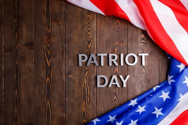 As palavras patriot day colocado com letras de metal prateado na superfície da placa de madeira com bandeira dos eua amassada