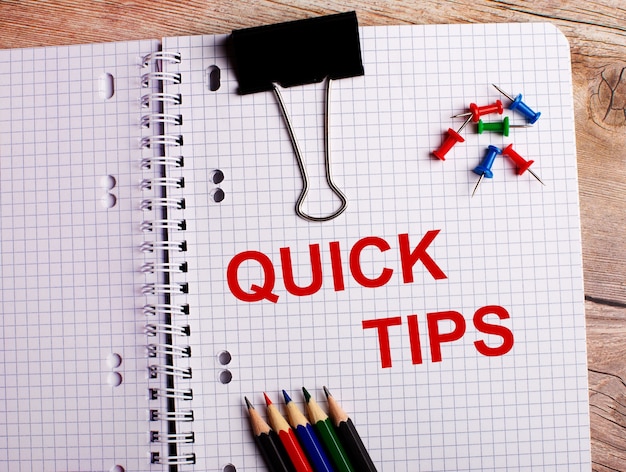 As palavras quick tips estão escritas em um caderno perto de lápis e botões multicoloridos em uma superfície de madeira