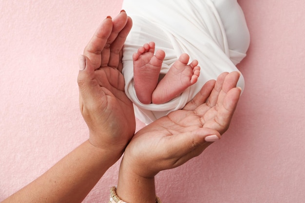 Foto as palmas das mãos do pai a mãe estão segurando o pé do bebê recém-nascido em um cobertor branco fundo rosa os pés do recém- nascido nas palmas das palavras dos pais foto dos dedos das mãos das crianças calcanhar e pés
