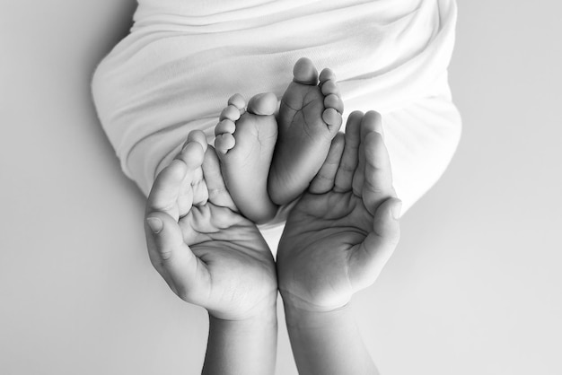 Foto as palmas das mãos do pai, a mãe segurando o pé do bebê recém-nascido, os pés do recém-natado nas palmas dos pais, estúdio macro foto em preto e branco de dedos das mãos, calcanhar e pés de uma criança.