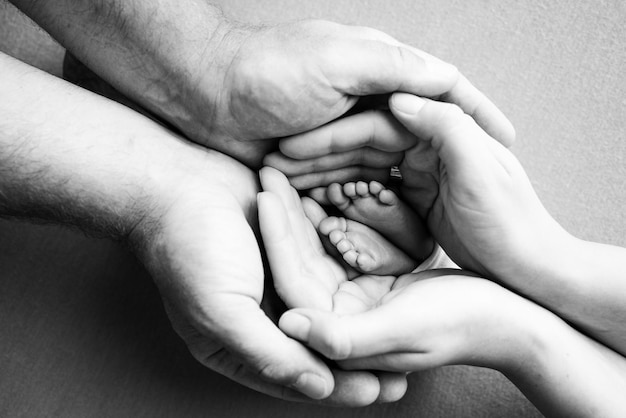 Foto as palmas das mãos dos pais um pai e uma mãe seguram os pés de um filho recém-nascido os pés de um recém-nascido nas mãos dos pais foto dos calcanhares e dedos dos pés preto e branco