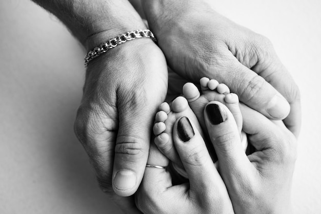 As palmas dos pais Um pai e uma mãe seguram um bebê recém-nascido pelas pernas Os pés de um recém-nascido nas mãos dos pais Foto de calcanhares e dedos do pé Foto macro de estúdio preto e branco