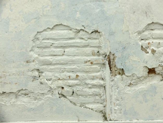 as paredes da casa são caiadas de branco com cimento lascado mostrando os tijolos. parede da casa velha
