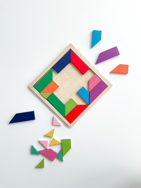 As peças multicoloridas do jogo Tangram são desmontadas na vista superior da mesa branca no fundo branco