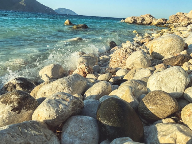 As pedras pequenas e grandes da costa do mar estão entre a água nas rochas da costa na areia da água