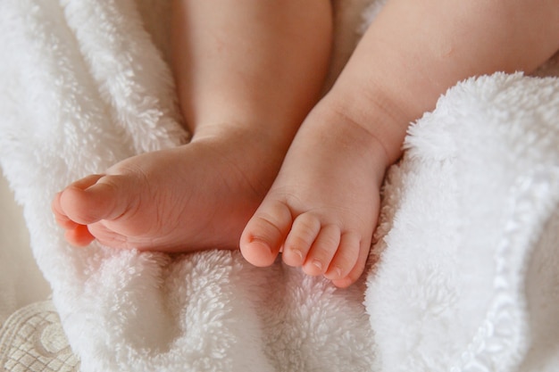 As pernas de um bebê recém-nascido deitado em um cobertor branco