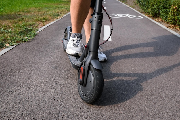As pernas de um homem de tênis branco em uma scooter elétrica preta sobre o asfalto