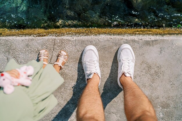 Foto as pernas de um pai e uma menina de pé na praia vista de cima cortadas sem rosto