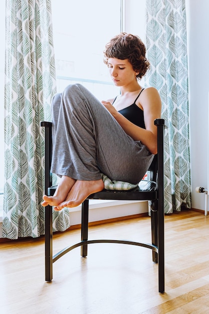 As pernas descalças de uma adolescente atraente se sentam na cadeira