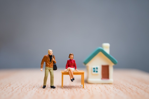 As pessoas, a mulher e o homem diminutos permanecem na frente da casa, uso para o conceito do trabalho em equipe do negócio