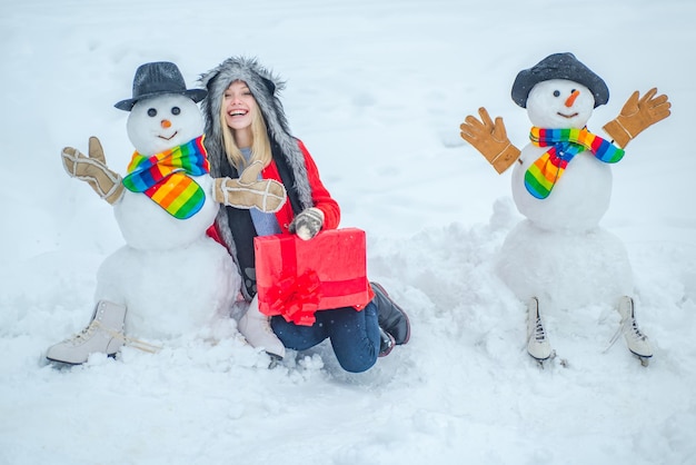 As pessoas adoram bonecos de neve bonitos de inverno com garota de inverno em pé na paisagem de Natal de inverno garota feliz com ...