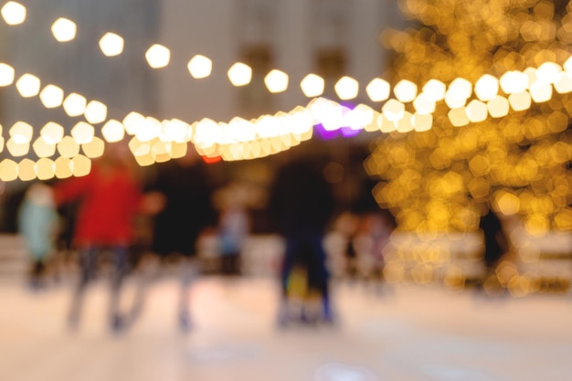 As pessoas andam na pista de patinação no fundo da árvore de natal na guirlanda leve papel de parede de imagem desfocada