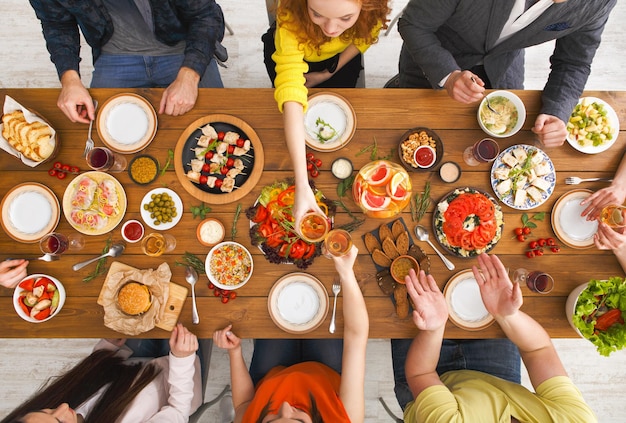 As pessoas comem refeições saudáveis na mesa festiva servida para a festa. Amigos comemoram com alimentos orgânicos na vista superior da mesa de madeira. Feliz companhia almoçando, comendo prato de salada
