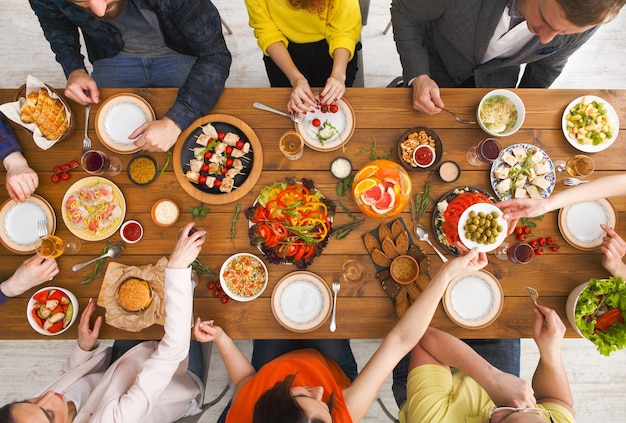 As pessoas comem refeições saudáveis na mesa festiva servida para a festa. Amigos comemoram com alimentos orgânicos na vista superior da mesa de madeira. Feliz companhia almoçando, comendo prato de salada