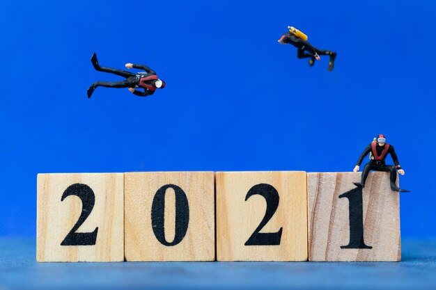 Foto as pessoas em miniatura mergulhando em torno de um bloco de madeira 2021 conceito de feliz ano novo